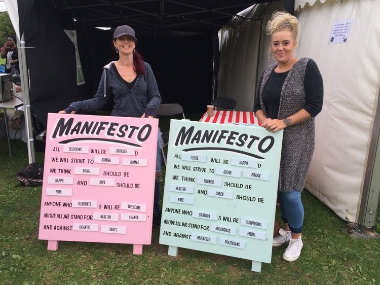 A picture of two women stood holding up Manifesto game boards
