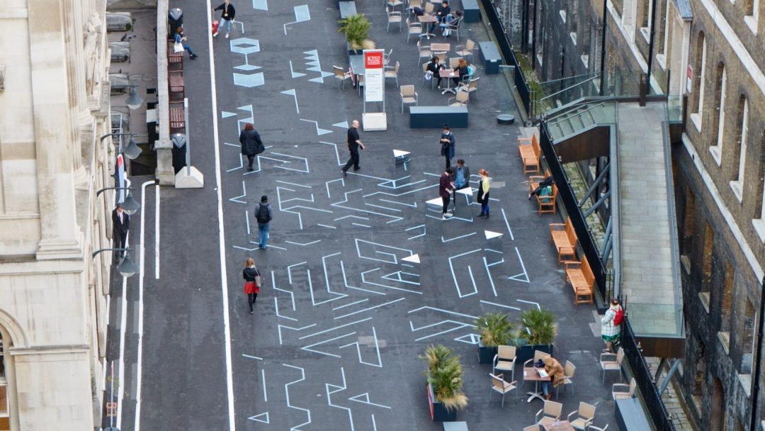 A picture of a pedestrian space taken from above, painted like a game board, on which people are playing