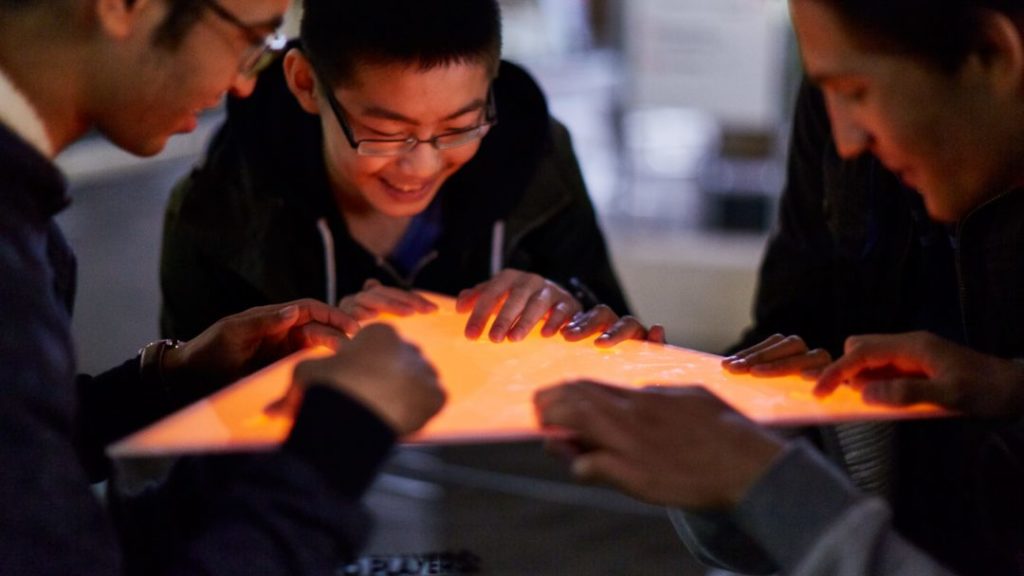 A picture of three people gathered around a glowing triangular block